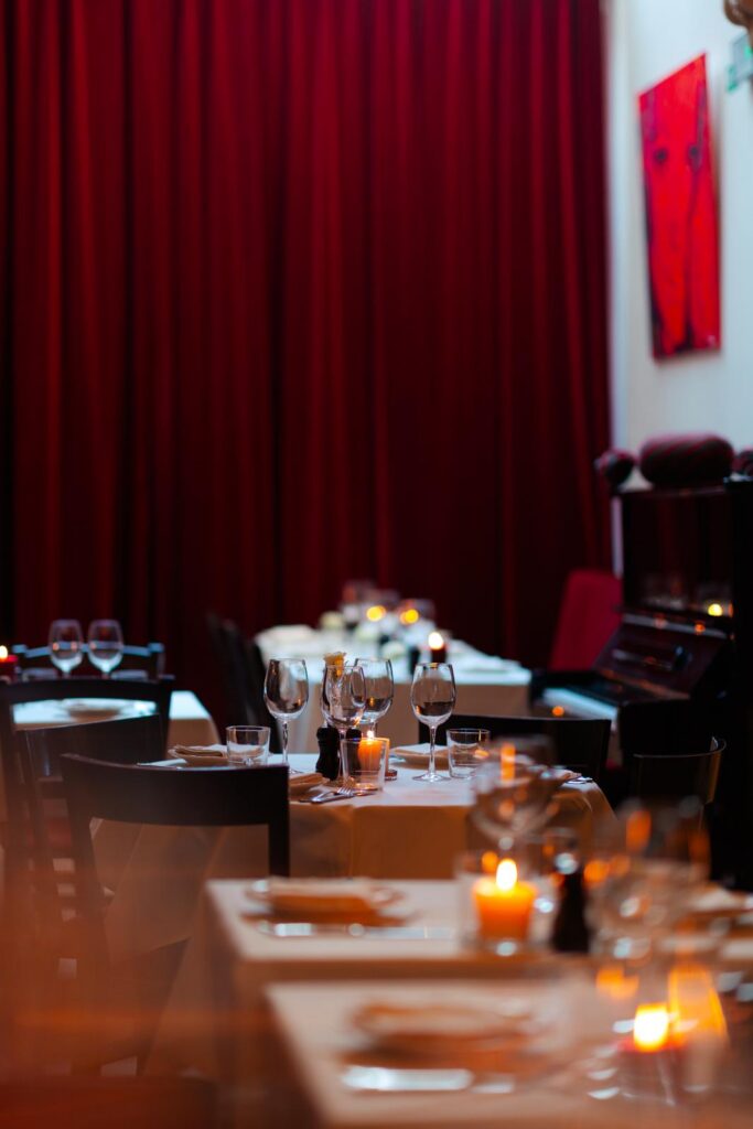 Gedekte tafels met kaarslicht en wijnglazen voor een dieprood gordijn in de eetzaal van BonBon